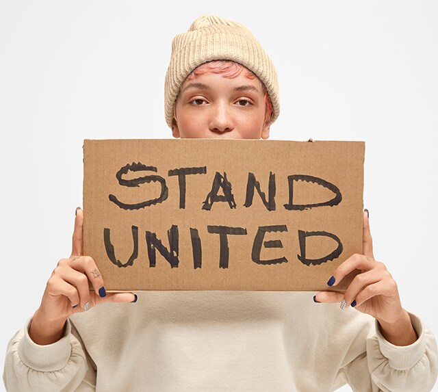Person posing with a cardboard sign that says Stand United